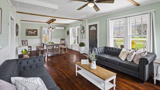 A spacious living room with a dark grey sofa, a wooden coffee table, and a ceiling fan. - Charming 4 bedroom farmhouse with large backyard for entertaining! (Mountain City)