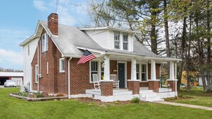 A two-story brick house with a white porch and an American flag. - Charming 4 bedroom farmhouse with large backyard for entertaining! (Mountain City)