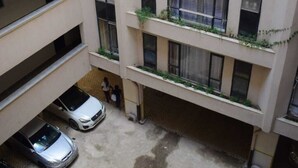 A multi-story building with balconies, a parking area with cars, and a visible water stain on the ground.