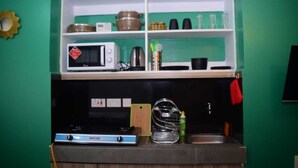 A kitchen with a microwave, stove, and shelves containing pots and kitchenware.