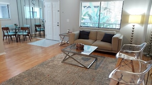 A living room with a sofa, coffee table, and clear chairs. There is a dining area with chairs and a table. - Stylish & comfy 2 bedroom condo centrally located (Tampa)