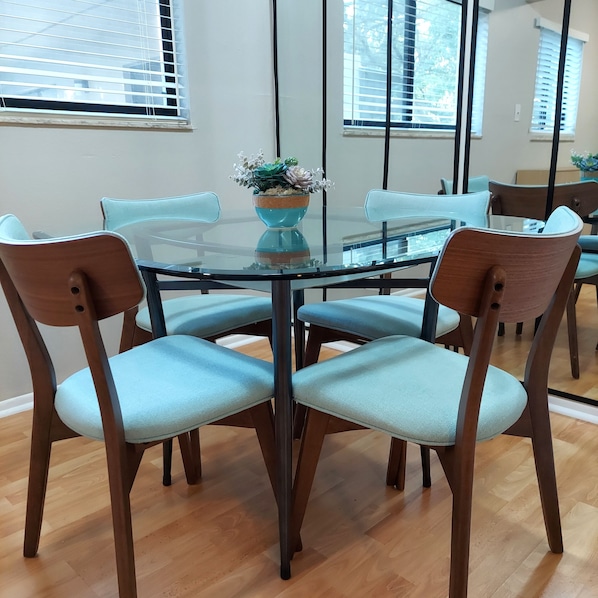 A round glass table with six chairs, each with a light blue cushion. A potted plant with white flowers is on the table. - Stylish & comfy 2 bedroom condo centrally located (Tampa)