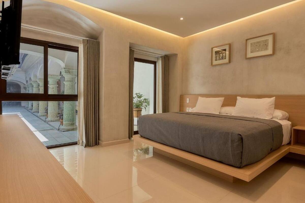 A modern hotel room with a large bed, a wooden bedside table, and a view of a courtyard with columns.