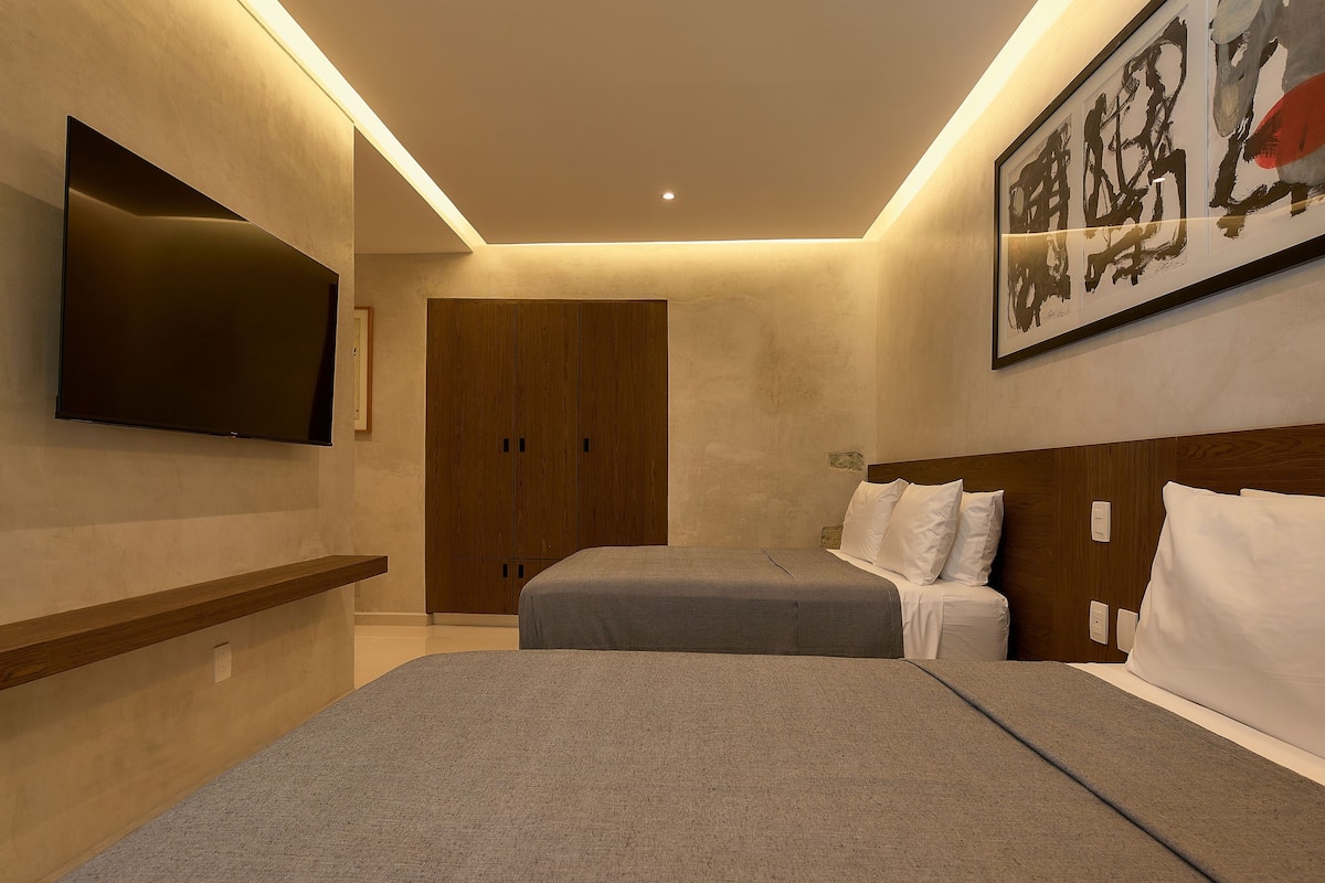 A modern hotel room with a flat-screen TV, two beds, wooden wardrobe, and a large abstract painting.