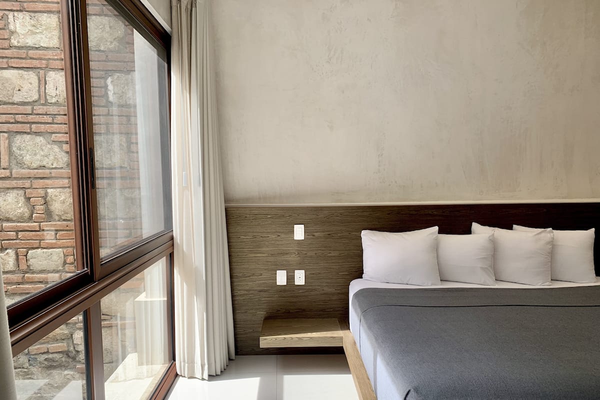 A bedroom with a large window, a wooden headboard, and a bed with white pillows.