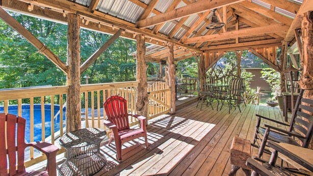 A wooden deck with a view of a swimming pool, surrounded by trees.