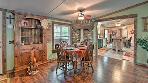 A dining area with a wooden table and chairs, a stone fireplace, and a kitchen in the background.
