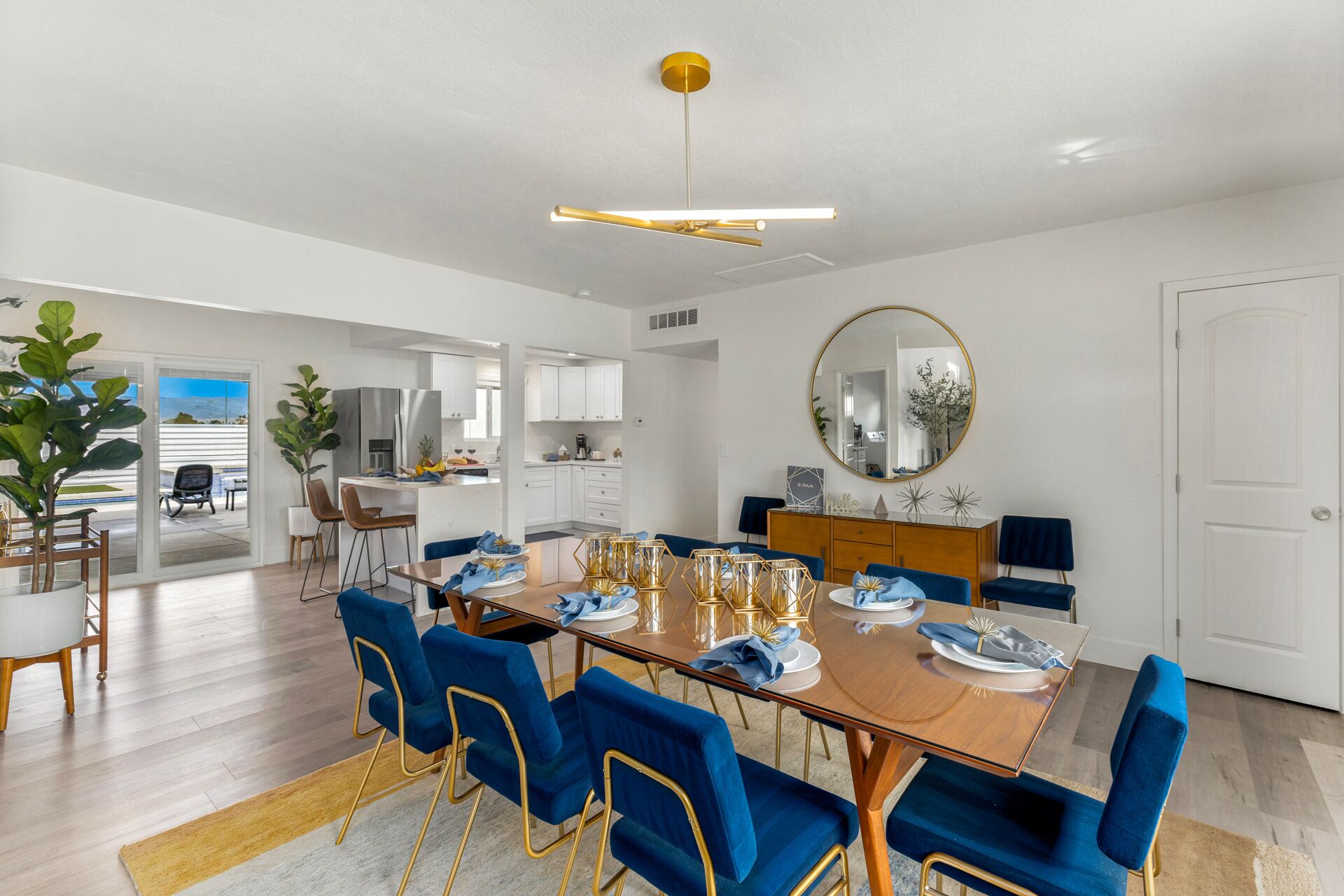 A modern kitchen with white cabinets, a stainless steel refrigerator, and a dining area with a wooden table and blue upholstered chairs.