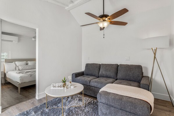A modern living room with a grey sofa, a round coffee table, and a ceiling fan. - Heated Pool & Spa & Games, Family & Pet Friendly, (Palm Desert)