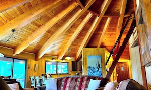 A wooden interior with a high ceiling, a dining area with chairs, a sofa, and a painting of a cactus.