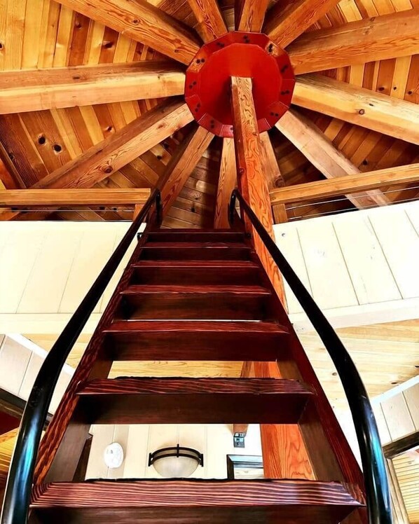 A wooden spiral staircase with a red central column, leading to a lower level.