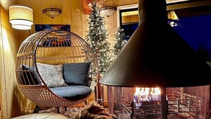 Een knus ingerichte kamer met een hangstoel, een zachte bank, een open haard en een kerstboom.