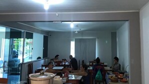 A dining area with tables and chairs, a ceiling fan, and a large window. - Pousada Boa Ventura (Anchieta)