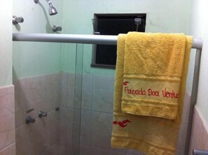 A bathroom with a yellow towel hanging on a metal rack, a shower, and a small window. - Pousada Boa Ventura (Anchieta)