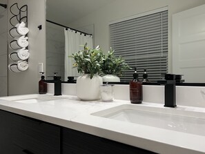 A bathroom with two sinks, a large mirror, a potted plant, and toiletries. - Modern Townhome- downtown Coeur d'Alene- minutes to waterfront restaurants shops (Coeur d'Alene)