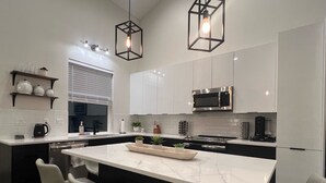 Une cuisine moderne dotée d’un îlot central, de meubles blancs, d’appareils électroménagers en acier inoxydable et de luminaires suspendus.