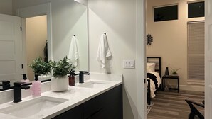 Une salle de bain moderne avec un grand miroir, deux lavabos et une plante en pot.