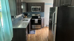 Une cuisine moderne avec des meubles de couleur sombre, des appareils électroménagers en acier inoxydable et un plancher en bois.