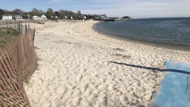Une plage de sable avec une clôture en bois sur la gauche et un ciel bleu dégagé.