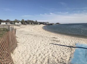 Una playa arenosa con una valla de madera a la izquierda y un cielo azul despejado.