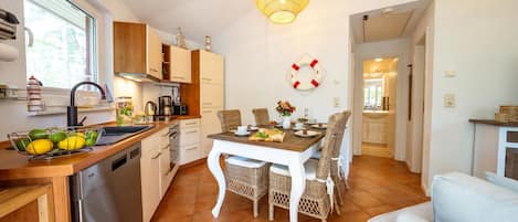 Une cuisine moderne avec des meubles blancs, une table à manger entourée de chaises en osier et un luminaire suspendu.