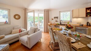 Un espacio de sala cómodo con un sofá y sillas, una mesa de comedor con platos y tazas, y una cocina con armarios y un lavaplatos.