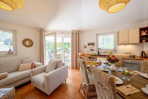 A cozy living area with a sofa and chairs, a dining table set with plates and cups, and a kitchen with cabinets and a sink.