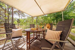 Une terrasse extérieure avec une table ronde en bois, deux chaises rembourrées et un grand auvent.