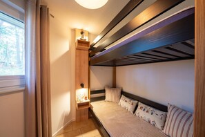 A compact room with a bunk bed, a small bedside table with a lamp, and a window with curtains. - Vacation home Tipi 365 - vacation home near the beach with terrace - Holiday home Tipi (Göhren)