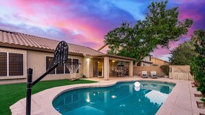 Un patio trasero con piscina, aro de baloncesto y zona de estar al aire libre con mobiliario.