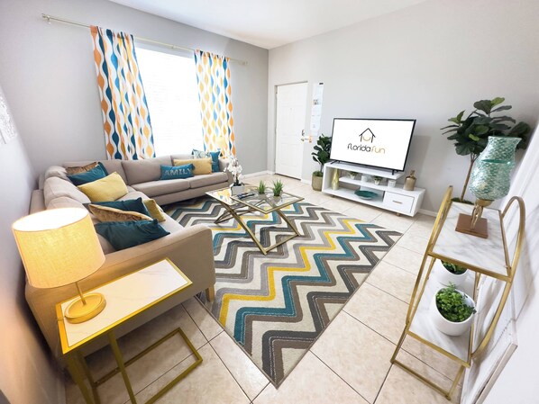 A modern living room with a sofa, coffee table, TV, and decorative plants.