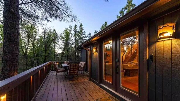 Une terrasse en bois avec des sièges extérieurs, un espace couvert offrant une vue sur l’intérieur, et un grand arbre situé à gauche.