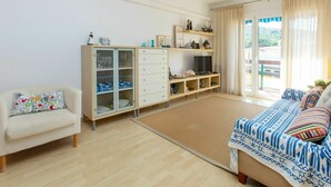 Une pièce bien éclairée, avec un canapé, un meuble avec des portes en verre, un téléviseur et un lit recouvert d’une literie à motifs.