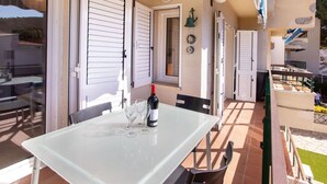 Une terrasse ensoleillée avec une table dressée pour deux personnes, une bouteille de vin et une cloche accrochée au mur.