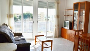 Ett vardagsrum med en soffa, ett soffbord, en tv placerad på ett träskåp och en skjutdörr i glas som leder ut till en balkong.