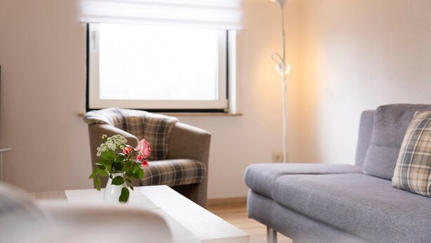 A modern living room with a grey sofa, a plaid armchair, and a white coffee table. - (STOE3) Holiday apartment "Waack" - Holiday apartment "Waack" up to 4 persons (Timmendorfer Strand)