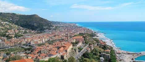 Un paysage urbain côtier avec une tour historique imposante, des bâtiments à étages et une vue dégagée sur la mer.