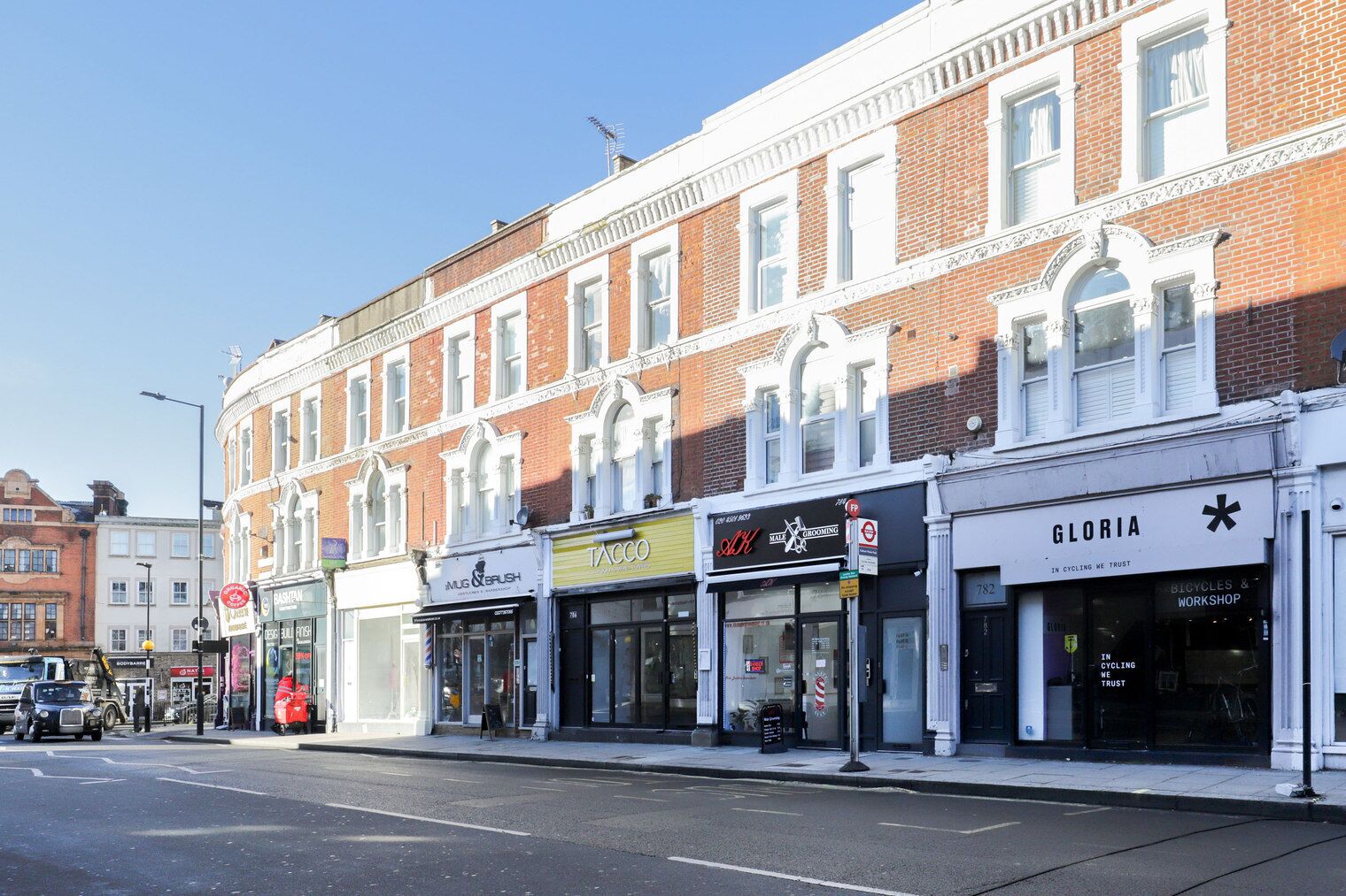 A row of shops with a prominent 'GLORIA' sign, a 'TACCO' shop, and a 'MALE & GROOMING' shop.