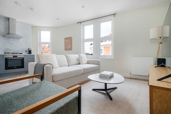 A modern living room with a sofa, a coffee table, and a kitchen area with an oven.