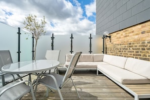 An outdoor patio with a round table, two chairs, a sofa, and a small tree.