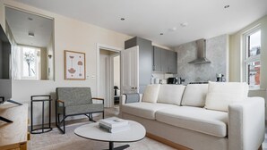 Een moderne woonkamer met een bank, fauteuil, salontafel en een keuken op de achtergrond.