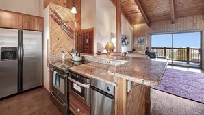 Une cuisine dotée de meubles en bois, d’appareils électroménagers en acier inoxydable, d’un plan de travail en granit et d’une grande fenêtre donnant sur une terrasse.