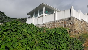 Um edifício branco com base de pedra, rodeado por folhagem verde densa.