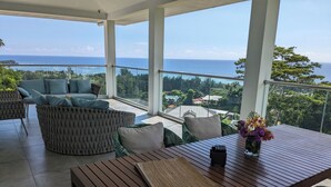 Uma varanda com mesa de madeira, assentos acolchoados e vista para o oceano.