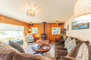 A cozy living room with a fireplace, wooden walls, a comfortable sofa, and a dining table. - Coastwood is a great coastal 4 bedroom house just minutes from the beach! (Fort Bragg)