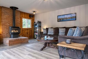 A cozy living room with a brick fireplace, a sofa set, a coffee table, and a bookshelf.