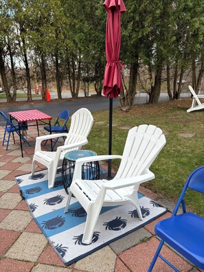 Eine Terrasse mit weißen Adirondack-Stühlen, einem roten Sonnenschirm und einer karierten Tischdecke.