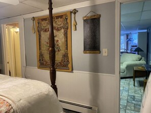 Ein Zimmer mit einem Bett, einem großen Wandteppich, einer Wandheizung und Blick auf einen Speisebereich.