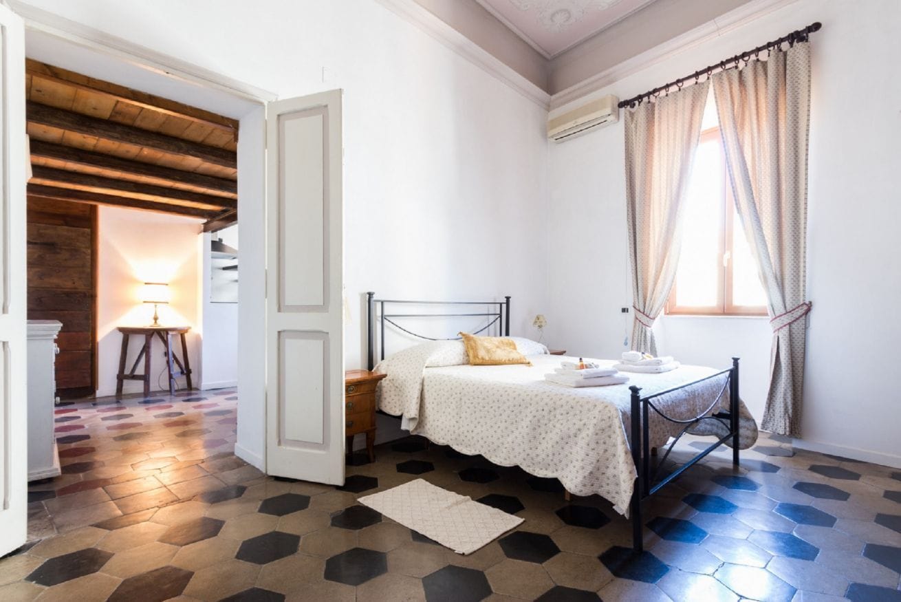Una camera da letto con un letto, un comodino, una lampada e una finestra con tende.
