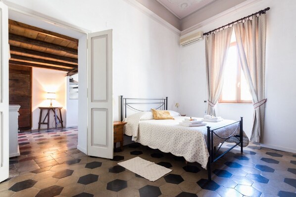 A bedroom with a bed, a nightstand, a lamp, and a window with curtains.